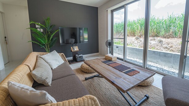 A modern living room with a sofa, coffee table, and a large window offering a view of a garden. - Guest House Terrace (Miyakojima)