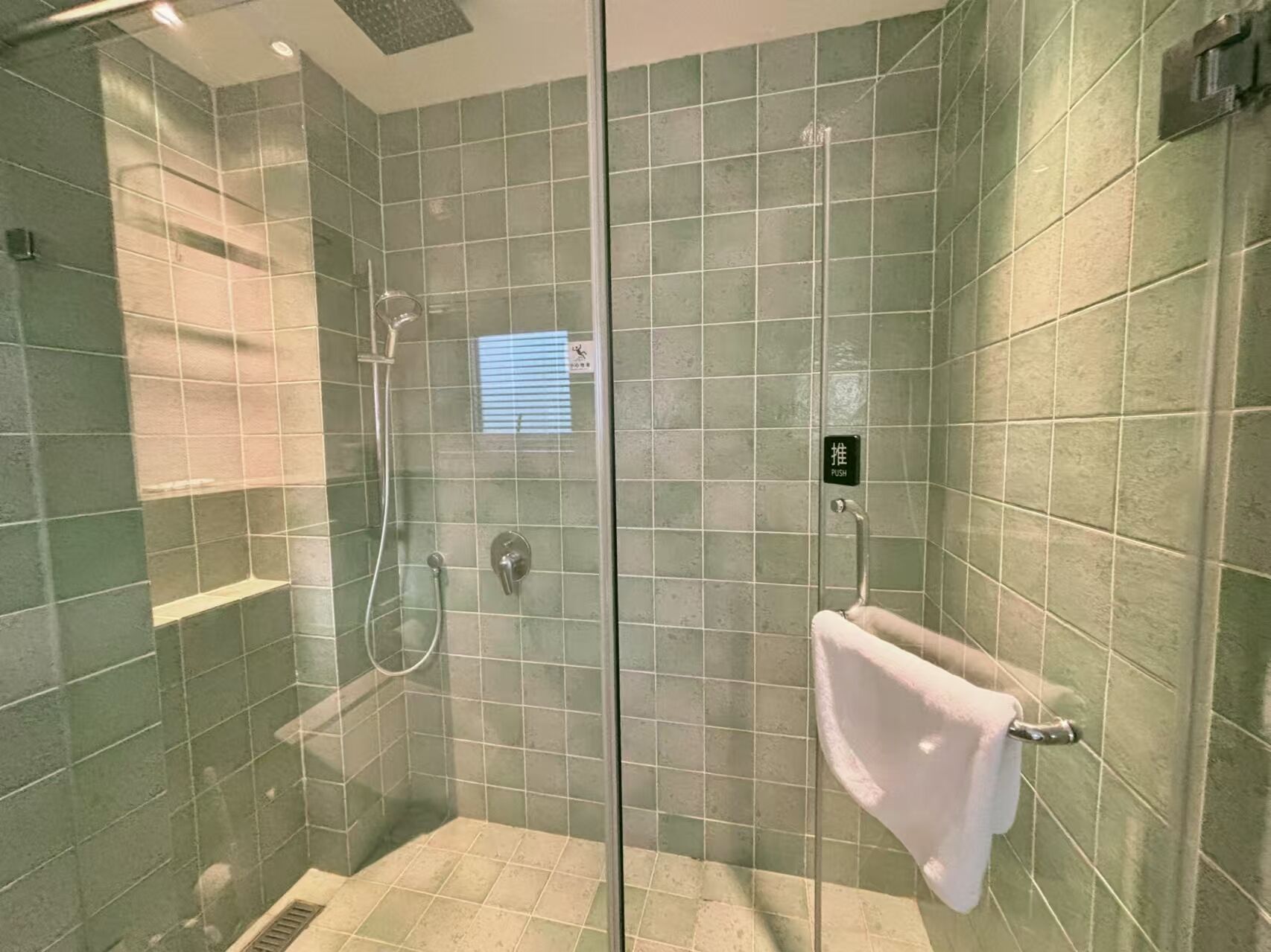 A glass-enclosed shower stall with a push button and a towel rack.