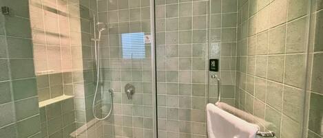 A glass-enclosed shower stall with a push button and a towel rack.
