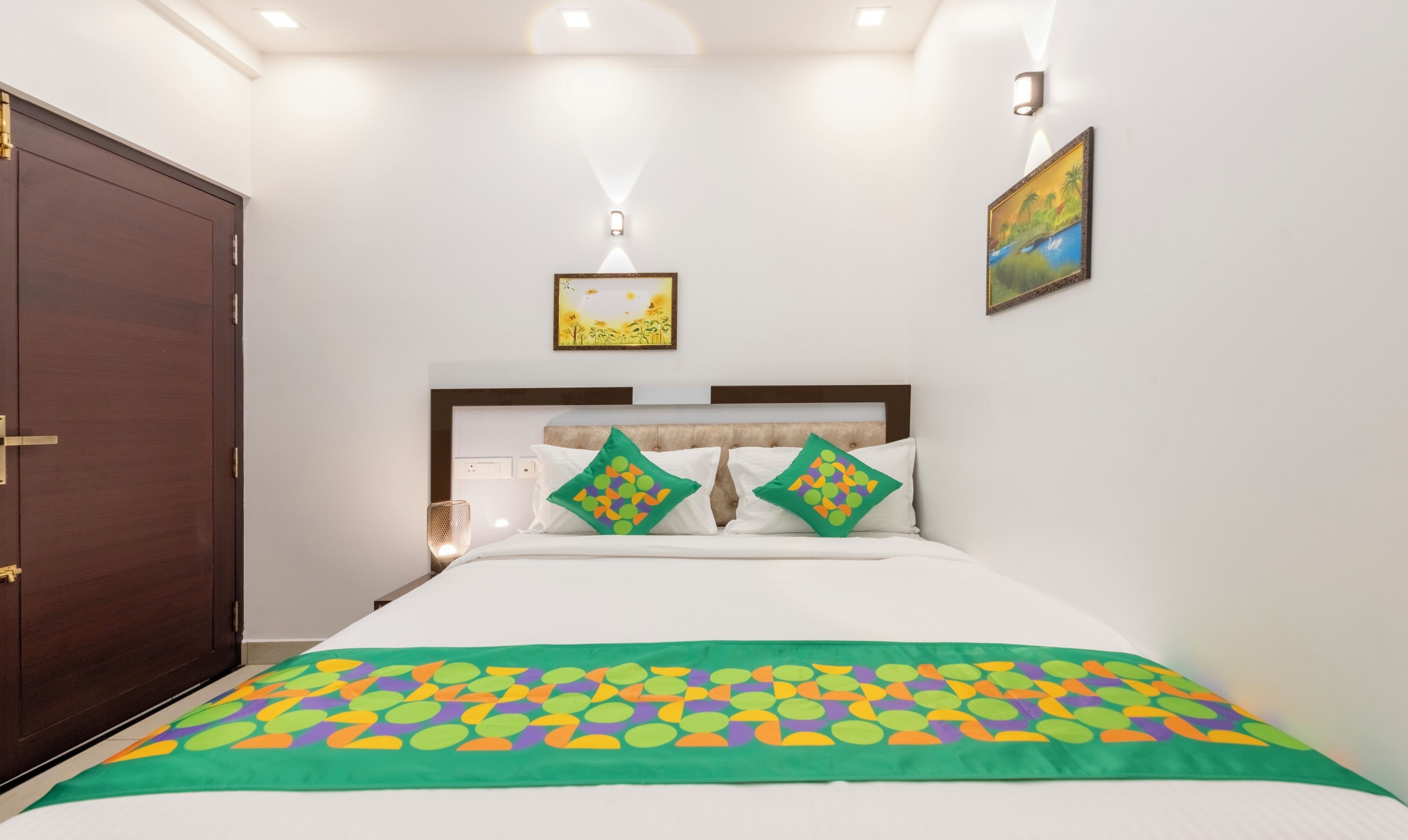A neatly arranged bedroom with a large bed, a wooden wardrobe, and two wall-mounted light fixtures.