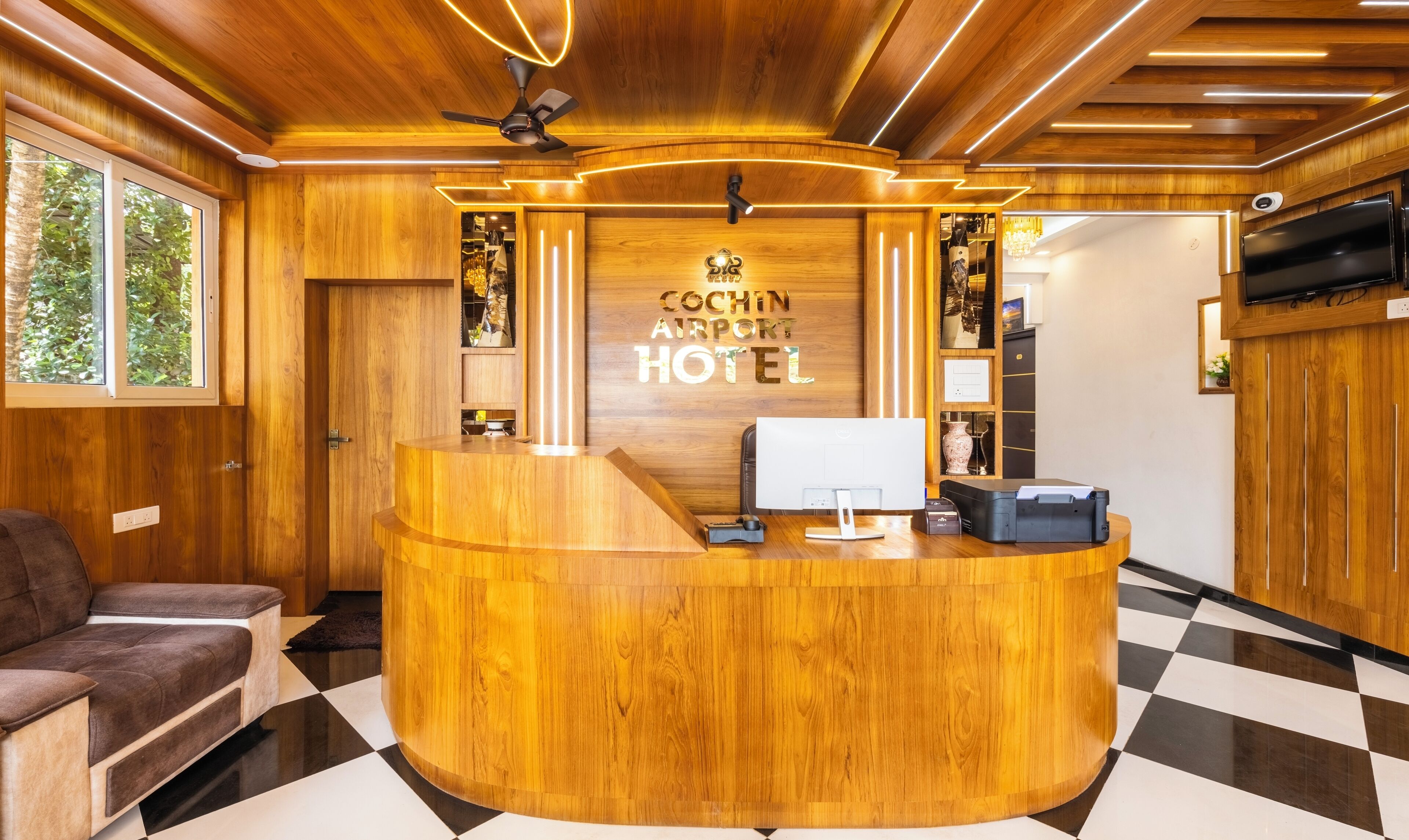 A reception desk with a wooden finish, a ceiling fan, and a sign reading "COCHIN AIRPORT HOTEL".