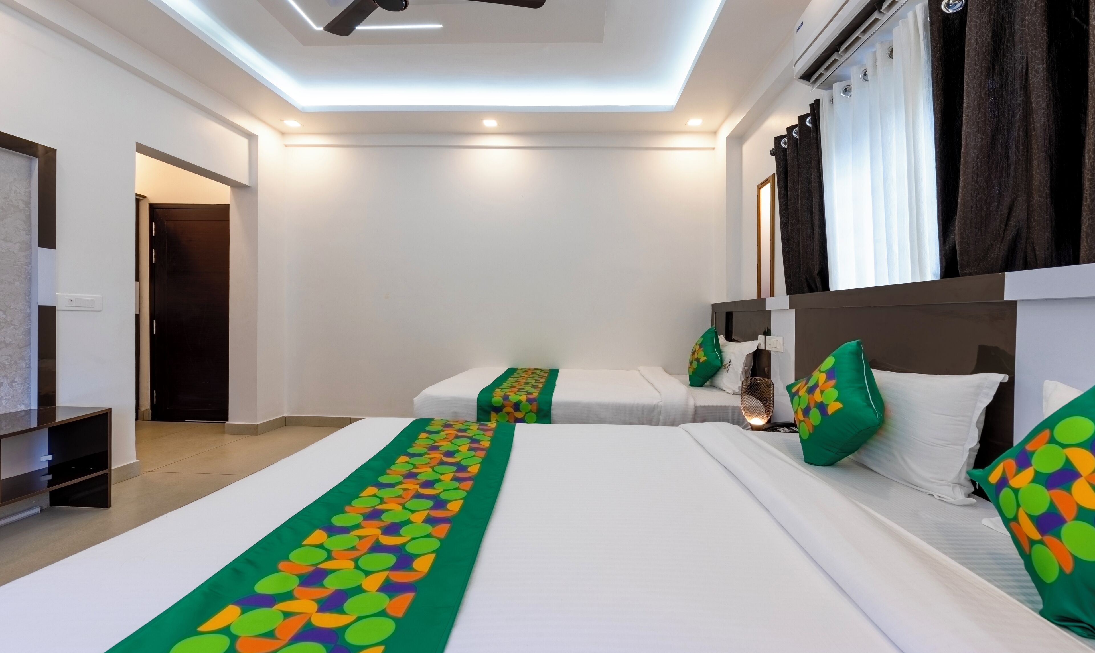 A hotel room with two beds, a ceiling fan, and a large window with curtains.