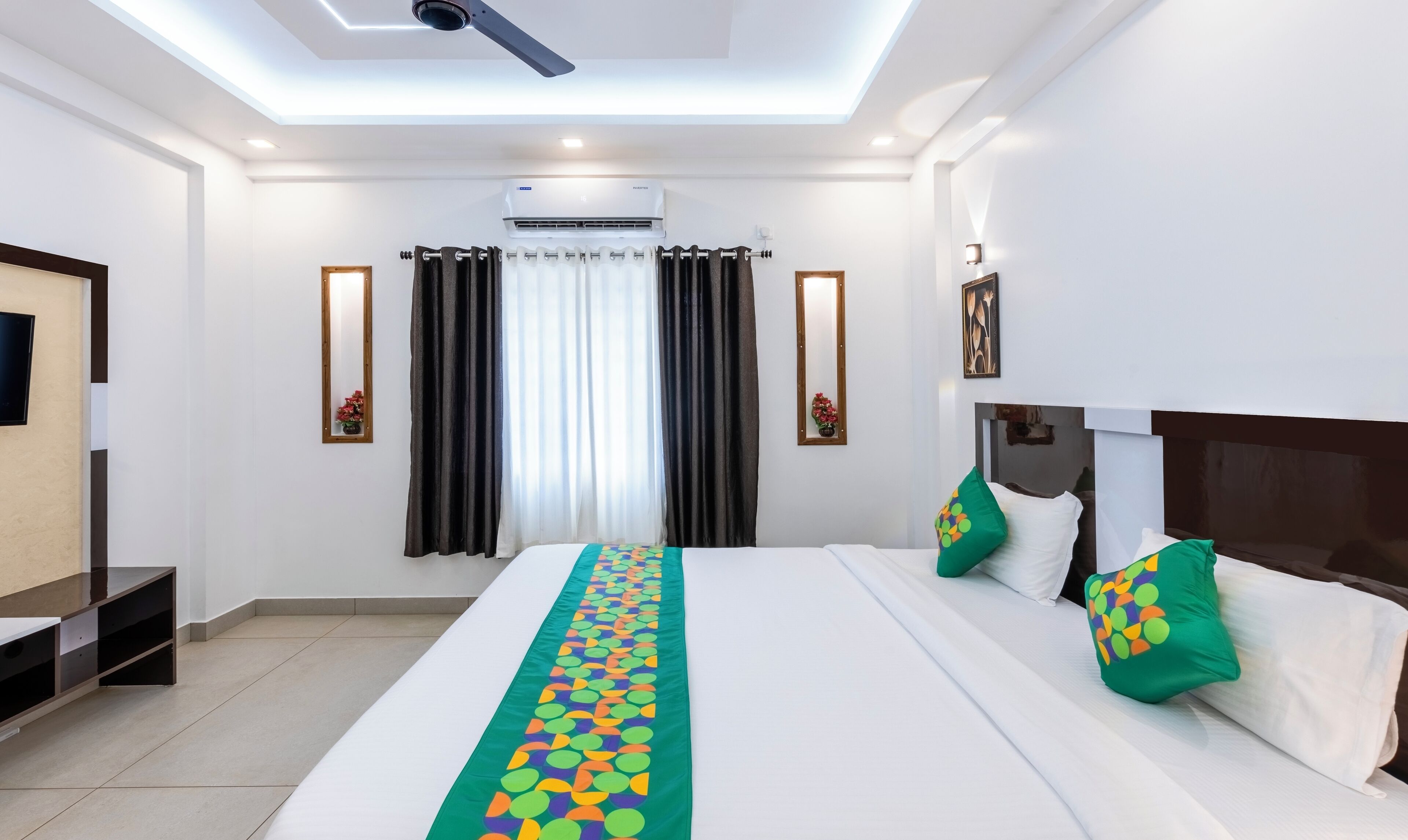 A hotel room with a large bed, a flat-screen TV, an air conditioning unit, and a ceiling fan.