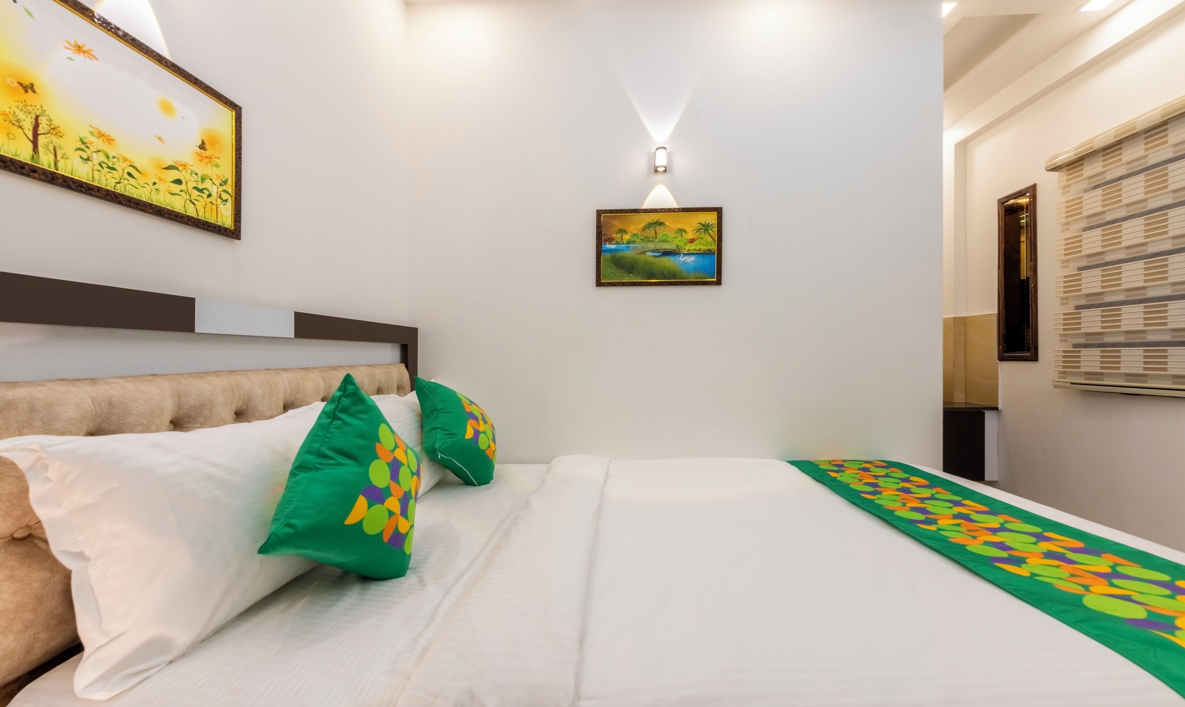 A neatly arranged bedroom with a bed, pillows, a painting, and a wall-mounted light.