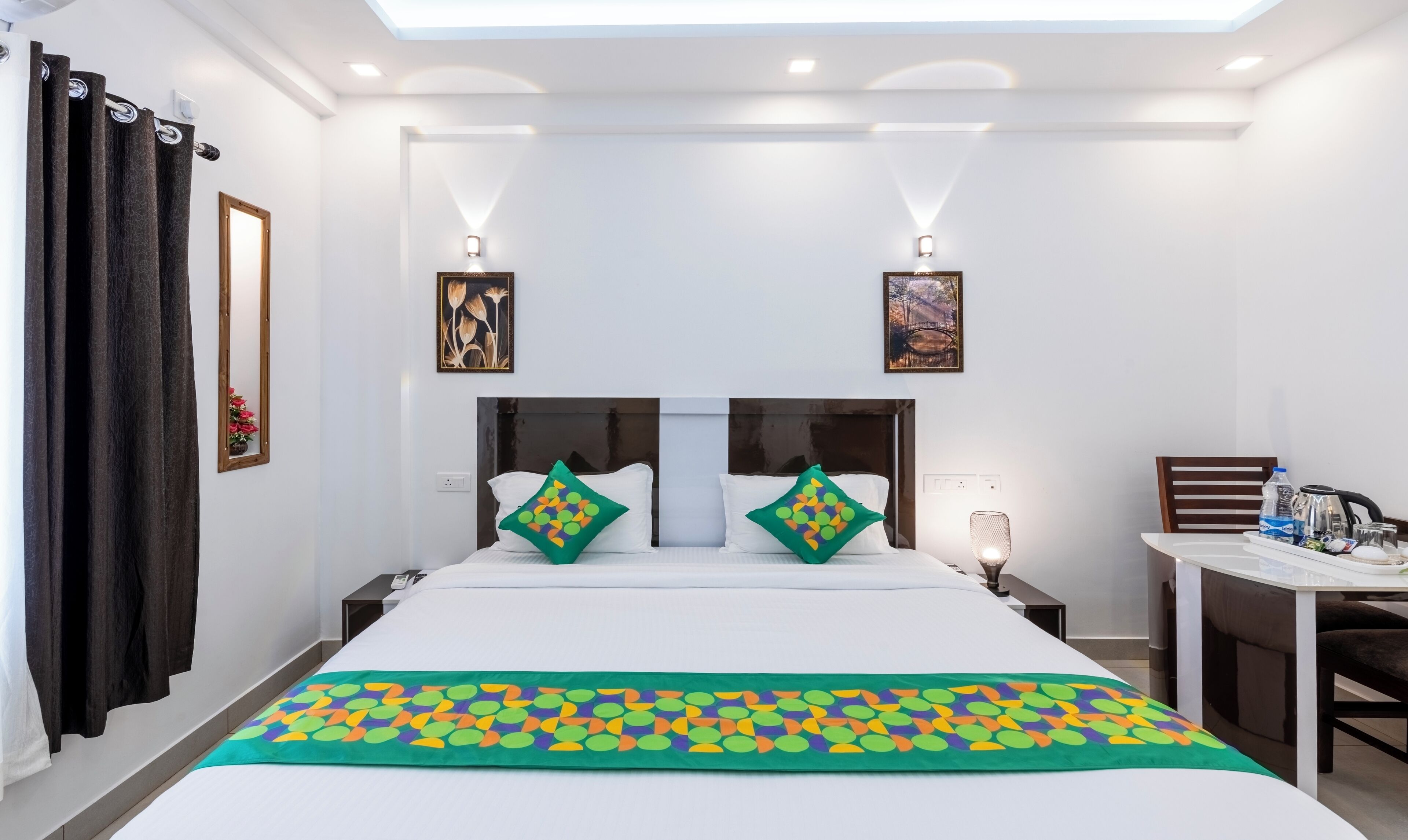 A hotel room with a large bed, two bedside tables, a desk with a chair, and artwork on the walls.