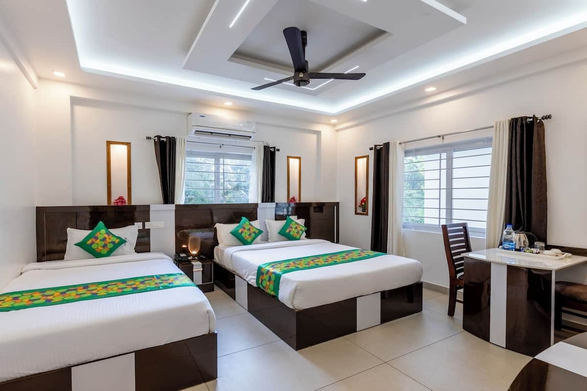 A hotel room with two beds, a desk, and a chair. There is a ceiling fan, an air conditioning unit, and a window with curtains.