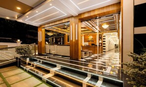 Un vestíbulo de hotel moderno con una recepción, una escalera de pasos iluminados y un candelabro.