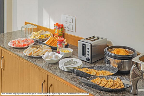 Mesa de desayuno tipo buffet con diferentes alimentos y un tostador.