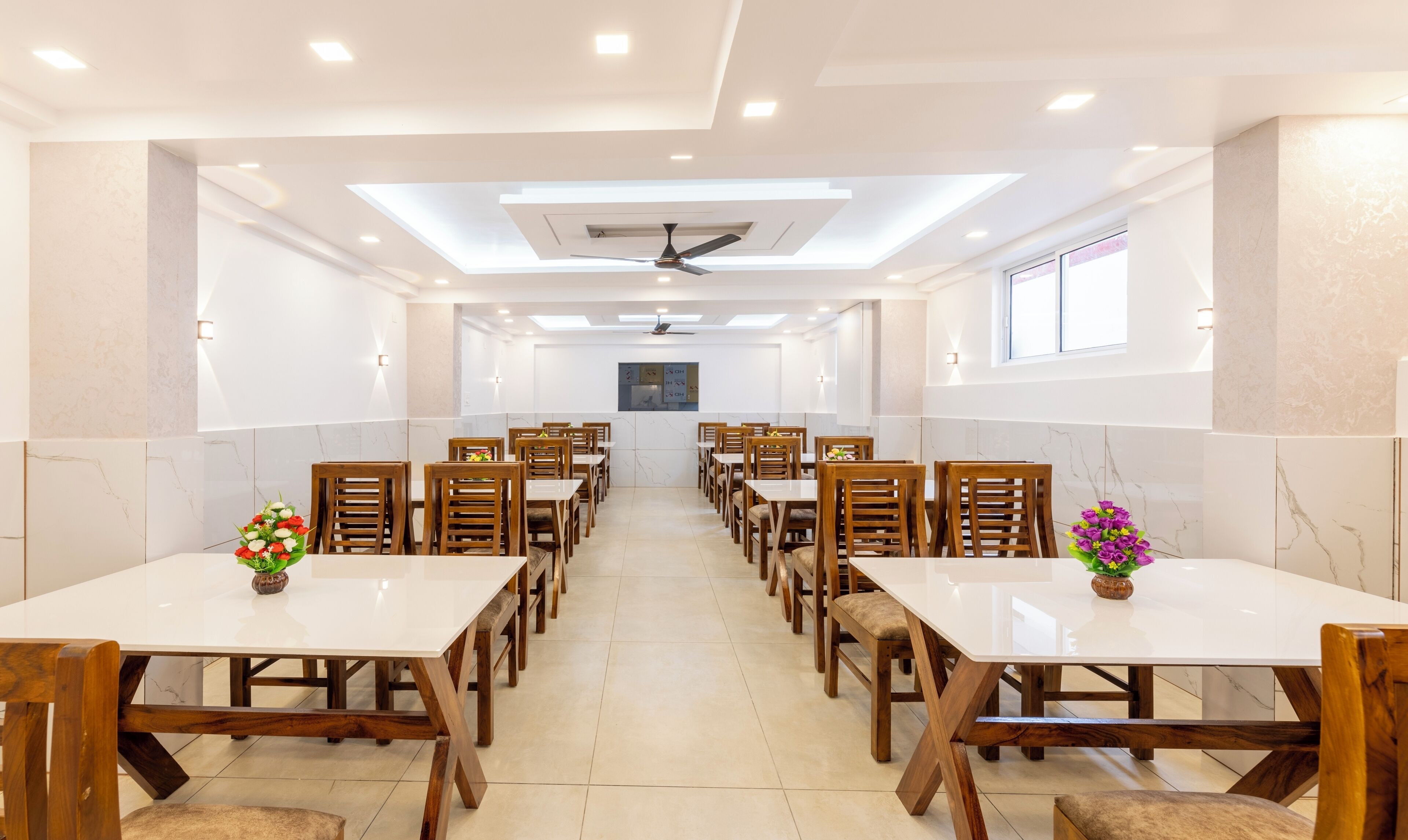 Un vaste espace dédié à la salle à manger, comprenant plusieurs tables et chaises, des ventilateurs de plafond et un éclairage encastré.