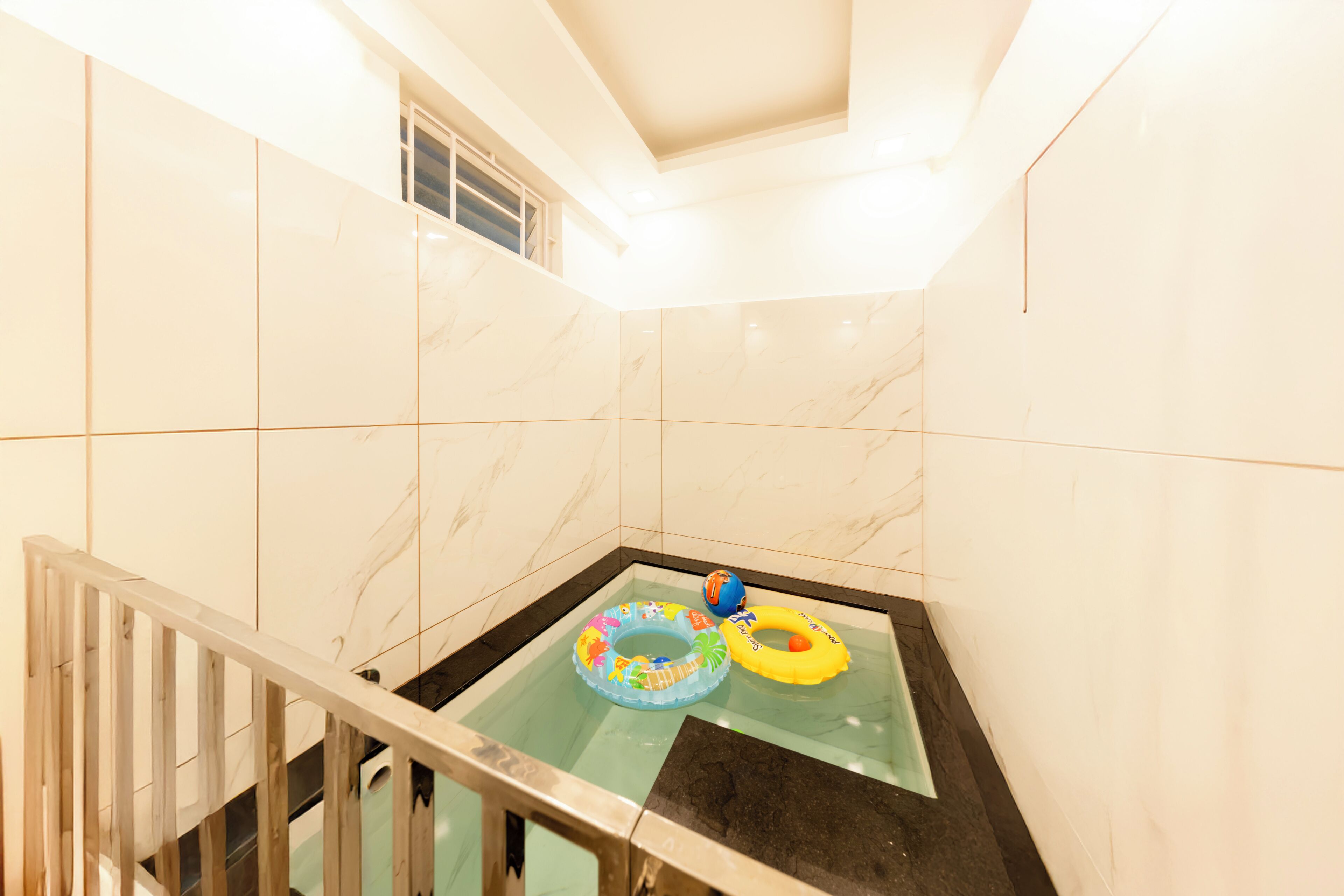 Un baño con paredes de mármol blanco, una bañera con mampara de vidrio y dos flotadores inflables de colores.