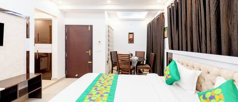 A hotel room with a bed, a desk, chairs, a ceiling fan, and a view of the outside.