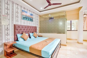A bedroom with a large bed, a ceiling fan, a nightstand, and a window with a view of palm trees. - Big House Inn  (Calangute)