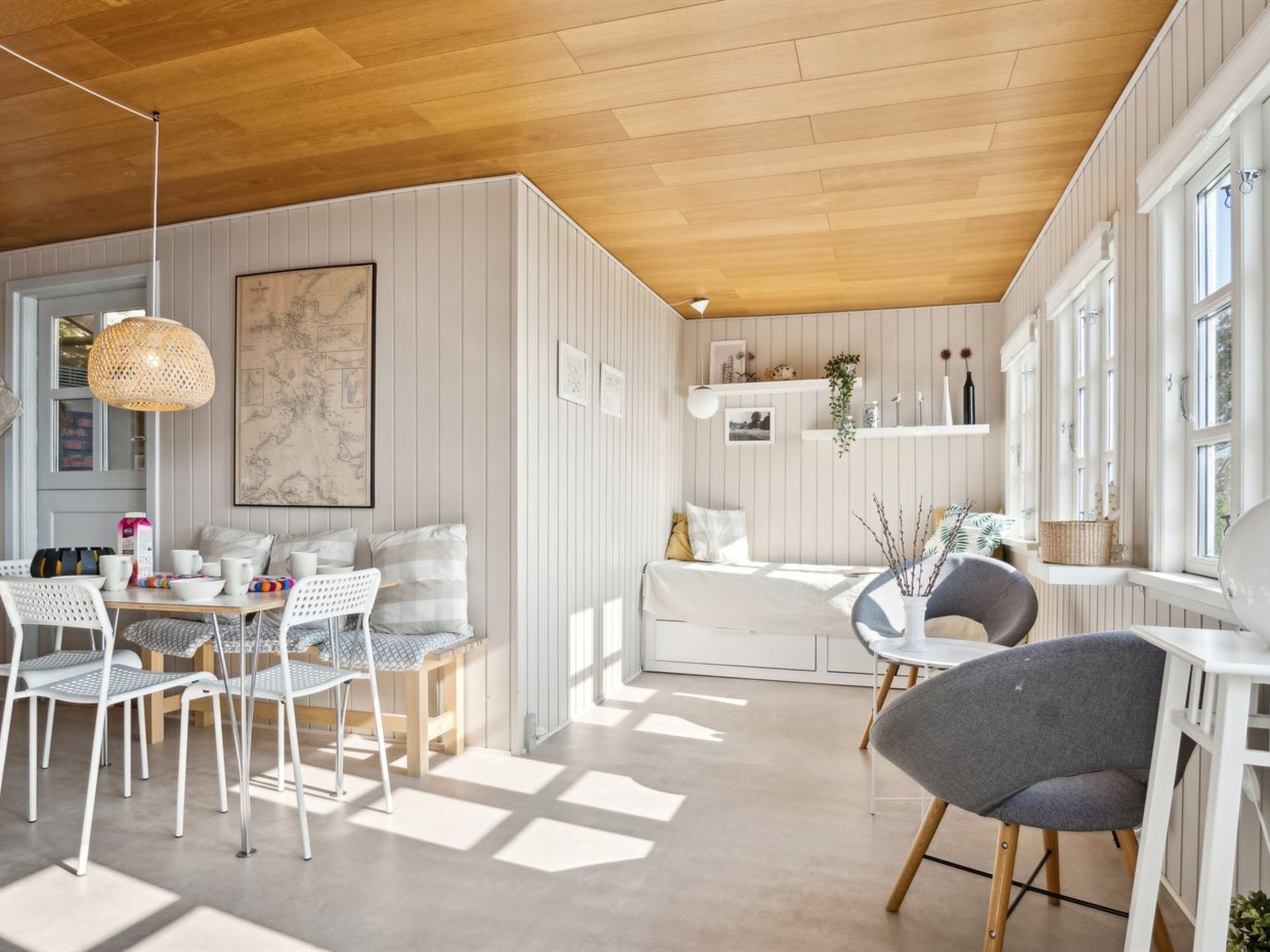 Un intérieur lumineux et moderne, avec un plafond en bois, des murs blancs et un coin repas comprenant des chaises et une table blanches.