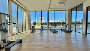 A spacious gym with large windows, exercise equipment, and a view of a building in the background.
