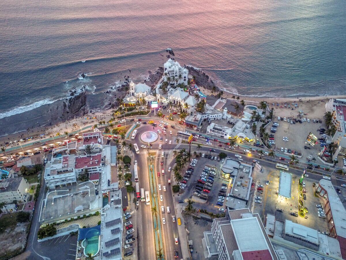 Vista aerea di una località costiera con una rotonda centrale, una chiesa e una spiaggia.