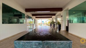 Un couloir agrémenté d’un élément décoratif aquatique réfléchissant, de murs en verre et de plantes en pot.