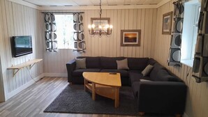 Uma sala de estar com um sofá escuro, uma mesa de centro de madeira, uma televisão sobre uma estante de madeira e um lustre.