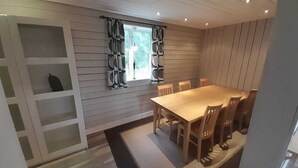 Uma área de refeições com mesa e cadeiras de madeira, uma janela com cortinas e uma estante embutida.