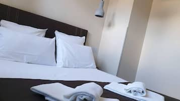 A neatly made bed with white linens and two folded towels on a dark-colored bedspread.