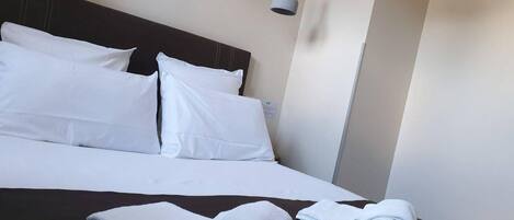 A neatly made bed with white linens and two folded towels on a dark-colored bedspread.