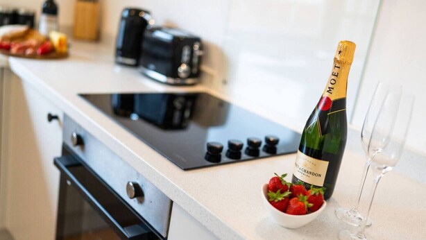 Una cucina con una bottiglia di champagne, una ciotola di fragole e due bicchieri da vino sul bancone.