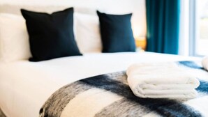 Un letto rifatto con precisione, coperto da lenzuola bianche e nere a righe, con due cuscini neri e un asciugamano bianco ripiegato su un cuscino rotondo.