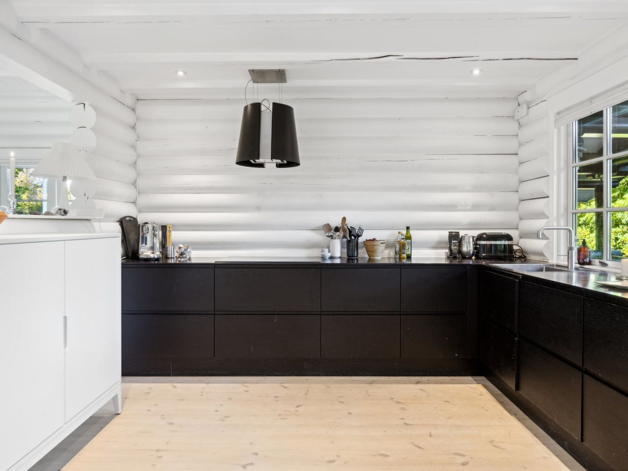 Une cuisine moderne avec un plan de travail noir, des armoires blanches et un luminaire suspendu.