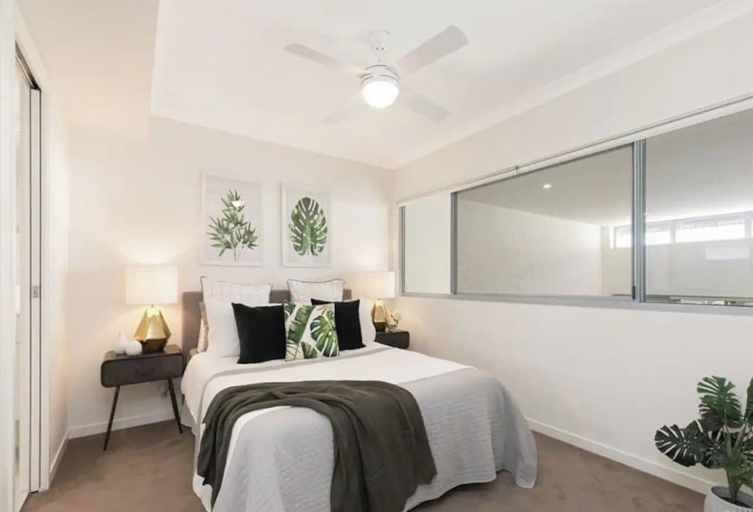 Ein Schlafzimmer mit Bett, Nachttischen, Deckenventilator und einem großen Fenster.