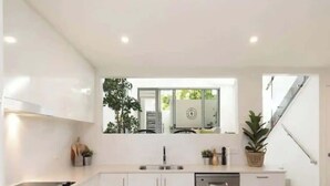 Een moderne keuken met witte kastjes, een spoelbak en een raam met uitzicht op een trap.