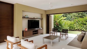 Ein modernes Wohnzimmer mit Flachbildfernseher, Holzmöbeln und Blick auf üppiges Grün.