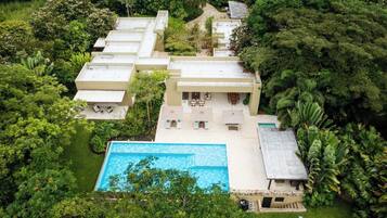 A multi-story building with a swimming pool, surrounded by lush greenery.
