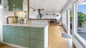 Una cocina moderna con gabinetes verdes, horno empotrado y zona de comedor con mesa y sillas de madera.
