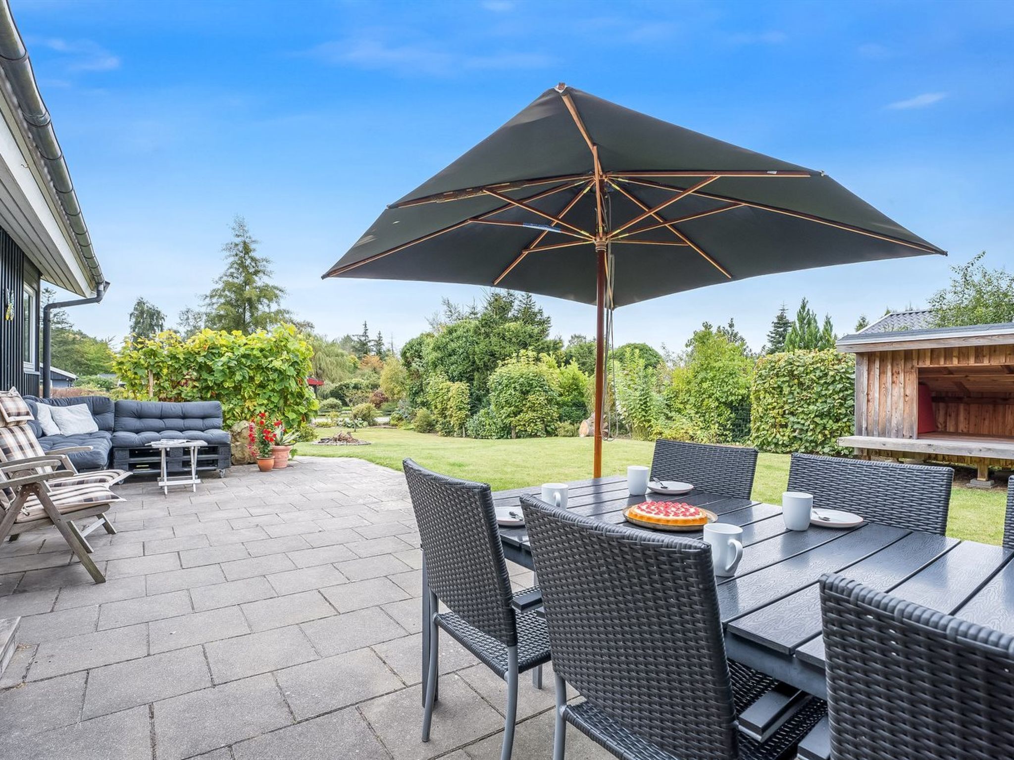 Een buitenterras met een eettafel, stoelen en een grote parasol.