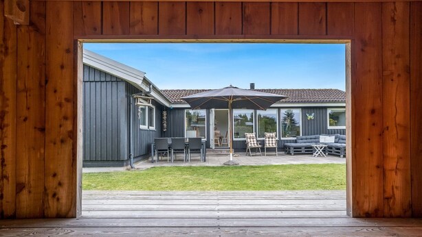 Una terraza de madera que conduce a un porche cubierto con mobiliario exterior y un paraguas grande.