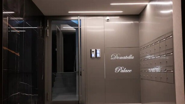 Ein moderner Aufzug mit Glastür, Bedienfeld und einem Schild mit der Aufschrift 'Donatella Place'.