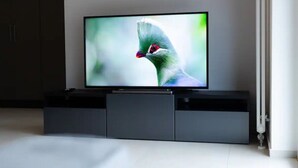 A flat-screen TV on a dark grey entertainment unit in a room with a white floor and a door on the right. - Cosy bilo close to the centre (Urban 2) (Lugano)