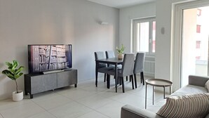 A modern living room with a flat-screen TV, a dining table with chairs, a sofa, and a potted plant. - Cosy bilo close to the centre (Urban 9) (Lugano)