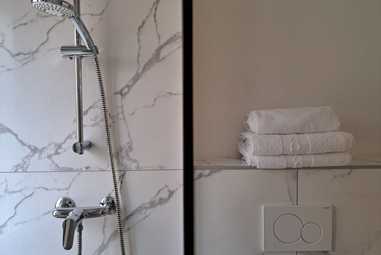 A bathroom with a shower, a towel rack, and a thermostat.