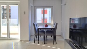 A modern living room with a dining table, chairs, a flat-screen TV, and a sliding glass door leading to an outdoor balcony. - Cosy bilo close to the centre (Urban 4) (Lugano)