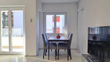 A modern living room with a dining table, chairs, a flat-screen TV, and a sliding glass door leading to an outdoor balcony.