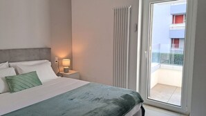A bedroom with a bed, nightstand, lamp, and a view of a balcony. - Cosy bilo close to the centre (Urban 4) (Lugano)