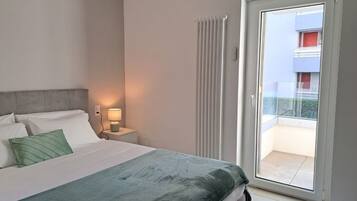 A bedroom with a bed, nightstand, lamp, and a view of a balcony.