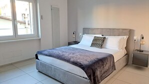 Une chambre moderne avec un grand lit, une table de chevet, une commode, une fenêtre et un radiateur.