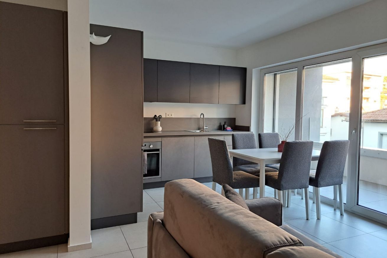 A modern apartment with a kitchenette, dining area, and a large sliding glass door to a balcony.