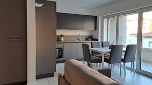 Un appartement moderne doté d’une kitchenette, d’un coin repas et d’une grande porte-fenêtre coulissante donnant sur un balcon.