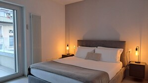 A modern hotel room with a large bed, two bedside tables with lamps, a sliding glass door to the balcony, and a radiator on the wall. - Cosy bilo close to the centre (Urban 5) (Lugano)