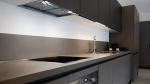 A modern kitchen with a central island, built-in oven, and stainless steel appliances. - Two-room apartment in new building in Lugano (Urban Residence 6) (Lugano)