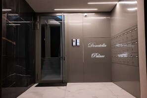 Ein moderner Aufzug mit Glastür, Bedienfeld und einem Schild mit der Aufschrift 'Donatella Place'.