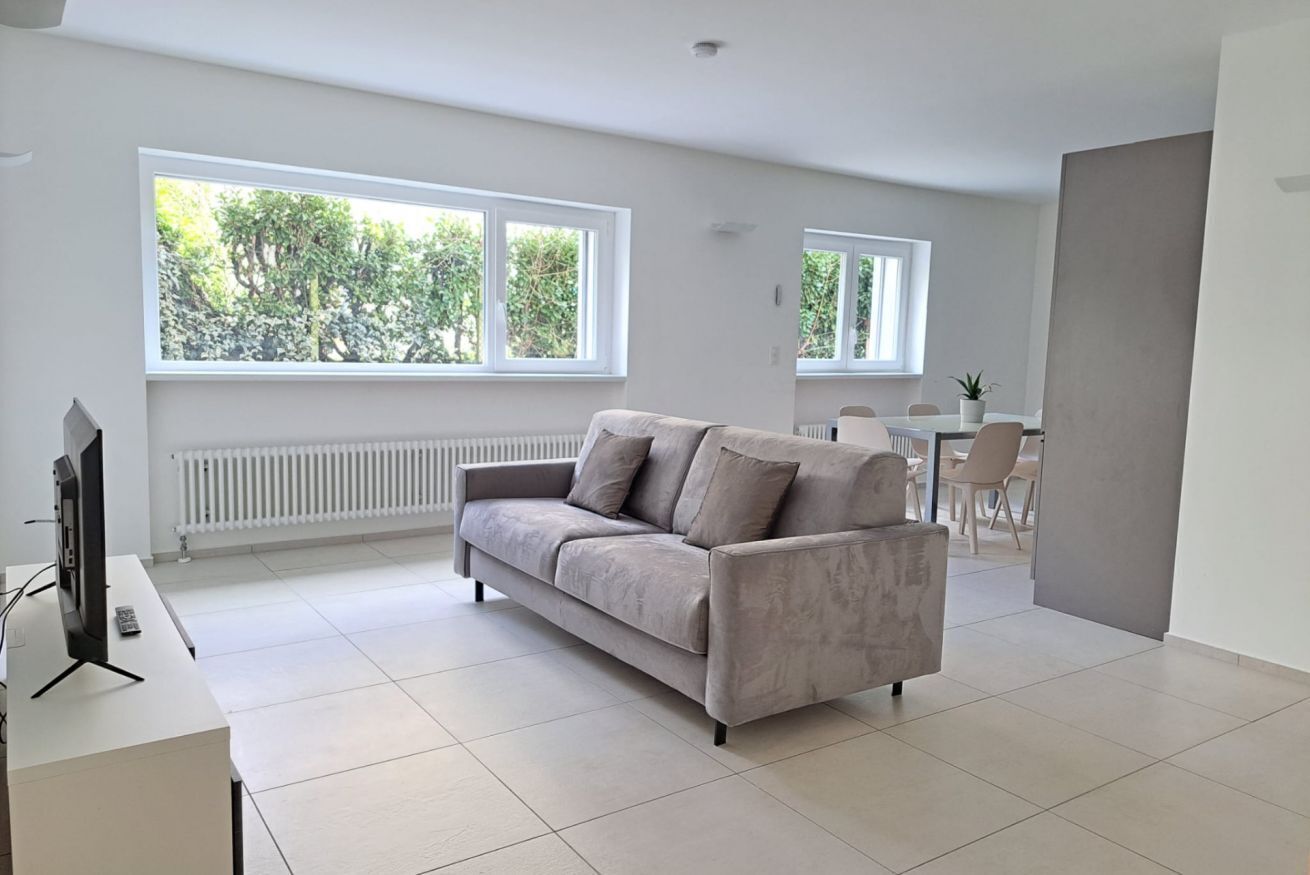 A modern living room with a sofa, a TV, and a dining area with chairs and a table.