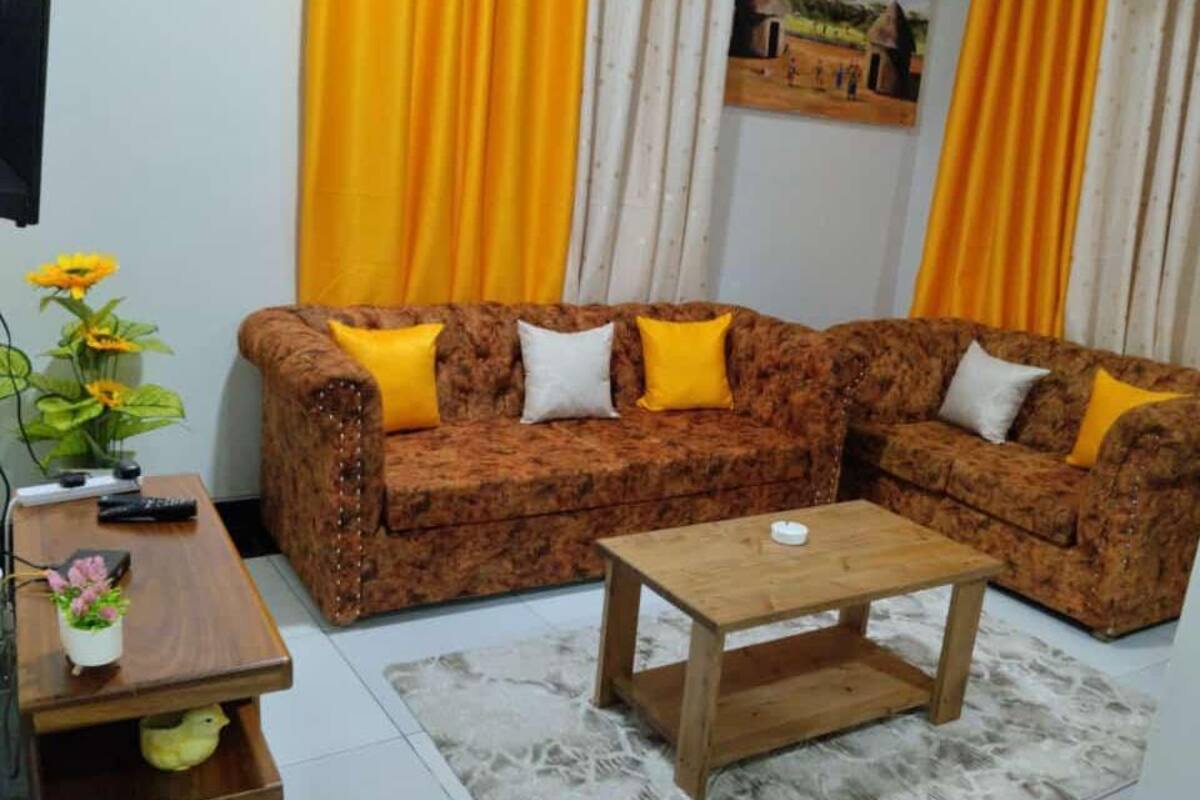 Un salon avec un canapé marron à motifs, des coussins jaunes, une table basse en bois et une petite plante posée sur une table d’appoint.